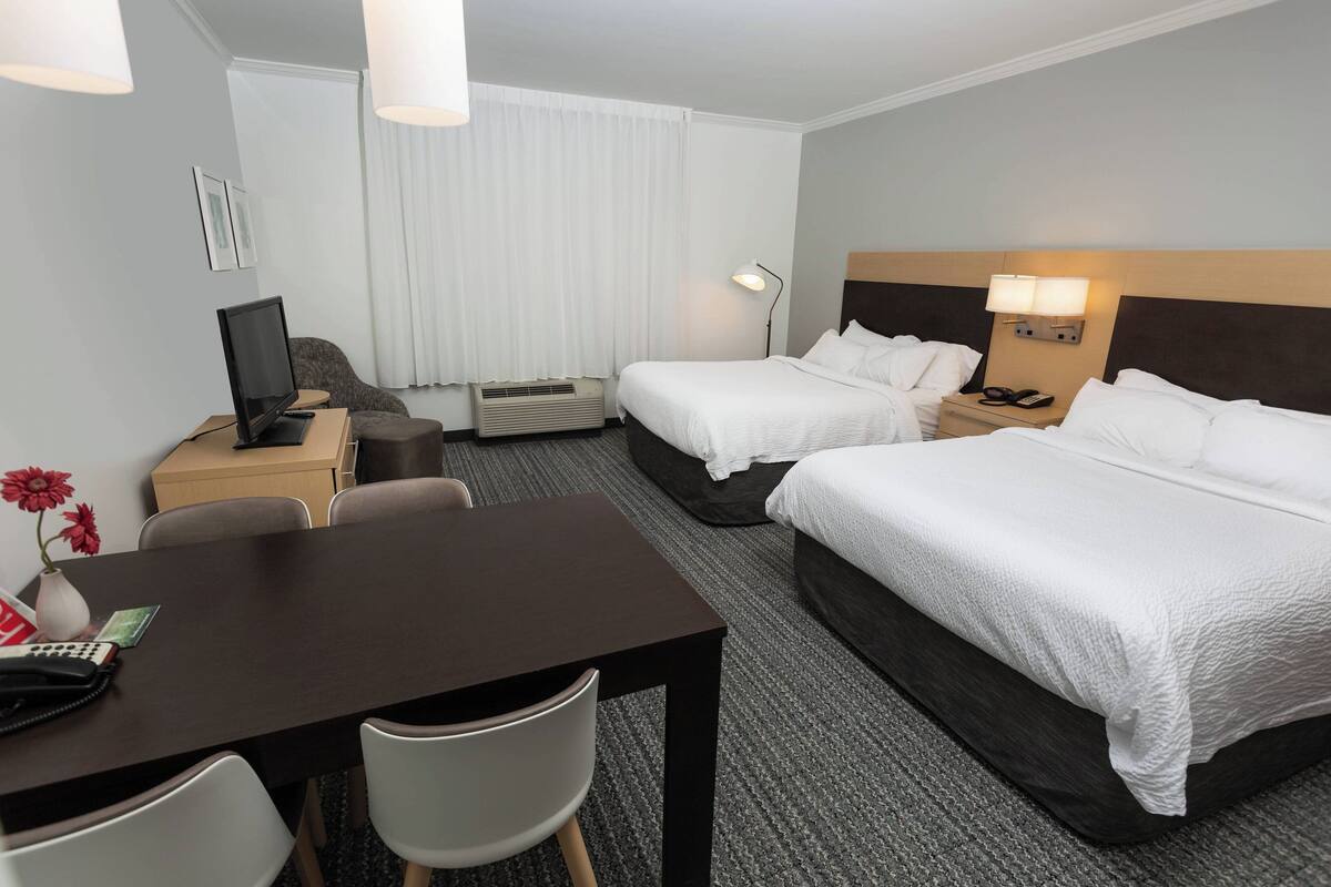 Ett hotellrum med två sängar, ett skrivbord med en stol, en TV, en lampa och ett fönster med gardiner.