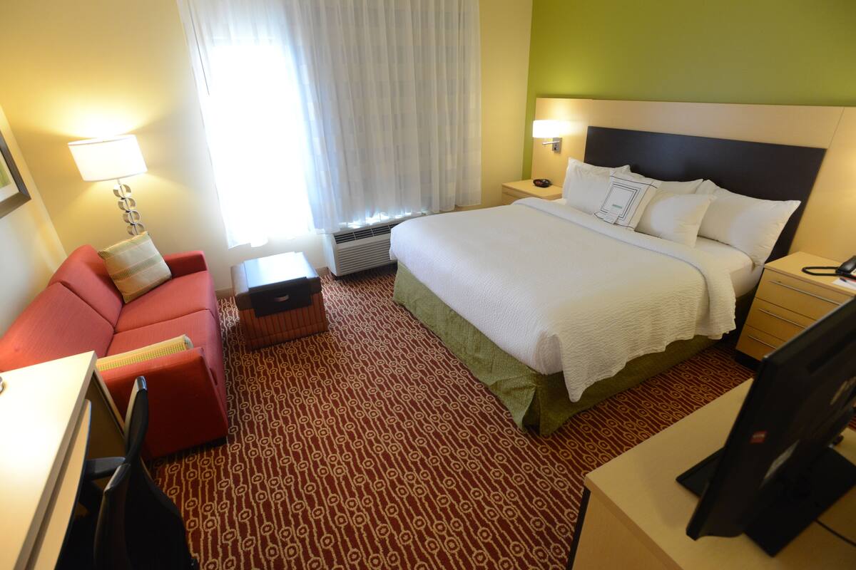 Ett hotellrum med en säng, en röd soffa, ett skrivbord, en lampa och en tv.