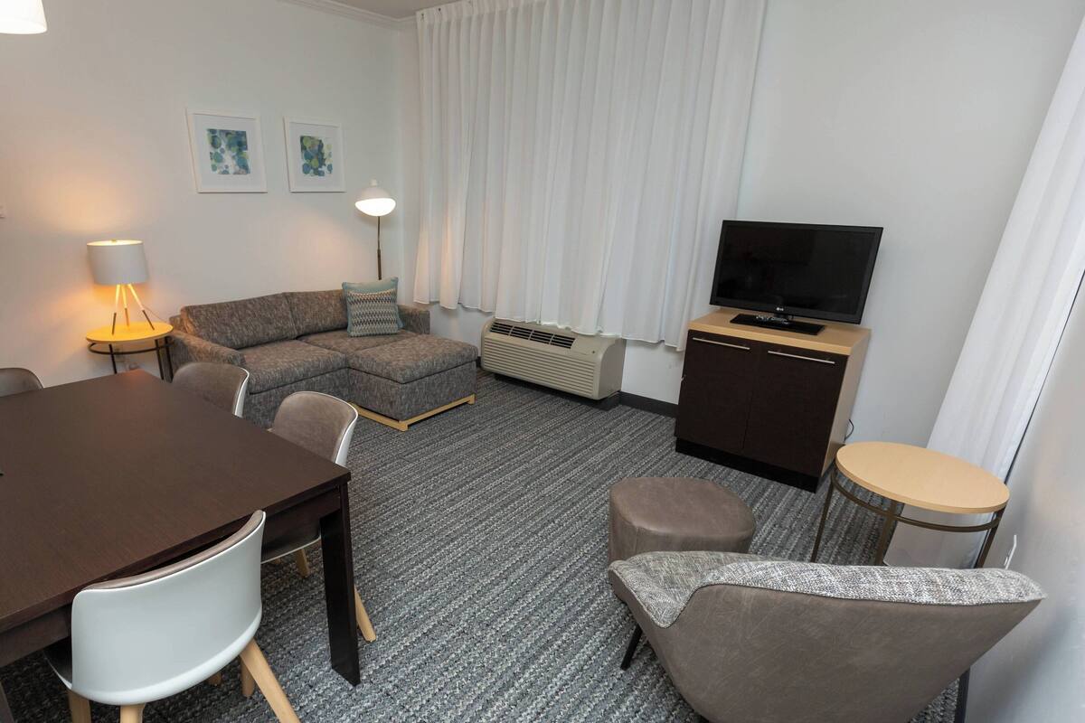 Ett hotellrum med en soffa, en TV, ett matbord och ett litet runt bord.