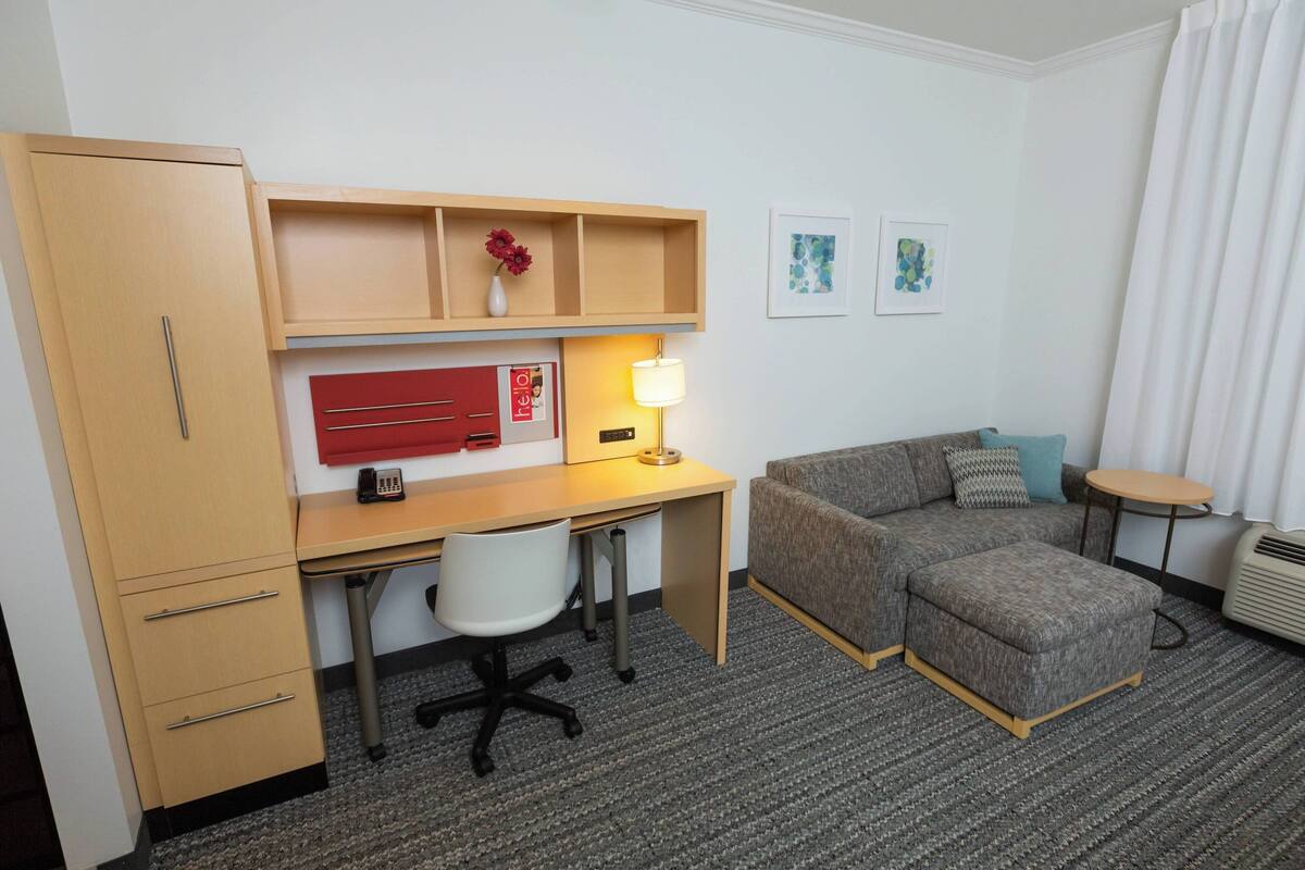 Ett hotellrum med ett skrivbord, en stol, en soffa, en pall och ett litet bord.