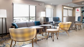 A modern hotel lobby with a sofa, chairs, tables, and a large window. - TownePlace Suites by Marriott Galveston Island (Galveston)