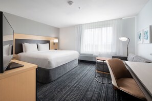 A modern hotel room with a large bed, a desk with a laptop, a sofa, and a small round table. - TownePlace Suites by Marriott Galveston Island (Galveston)
