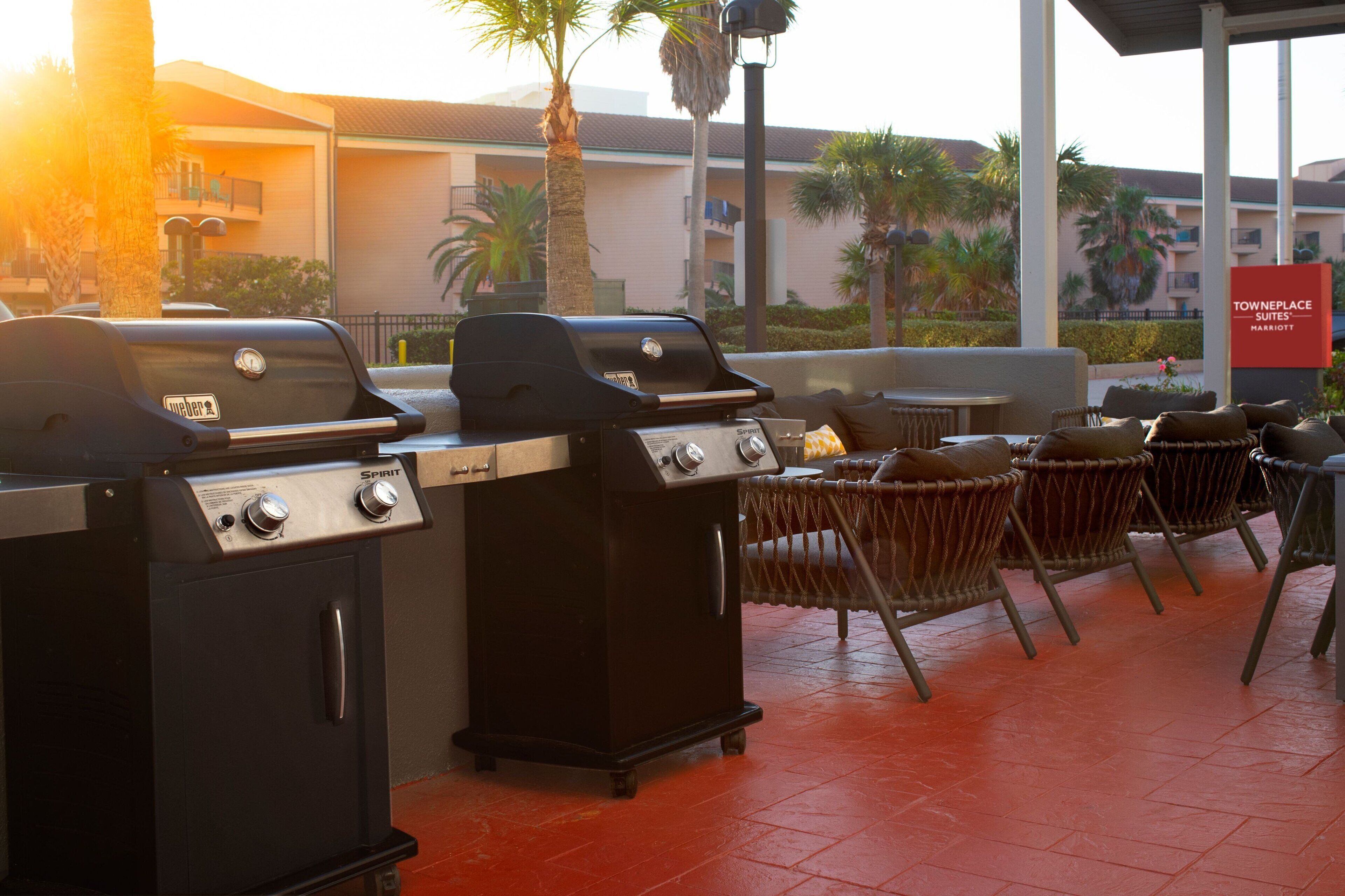 An outdoor patio area with two barbecue grills, wicker chairs, and a view of a hotel building.