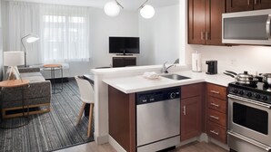 A modern kitchen with a dishwasher, stove, microwave, and a small dining area with a table and chairs. - TownePlace Suites by Marriott Galveston Island (Galveston)