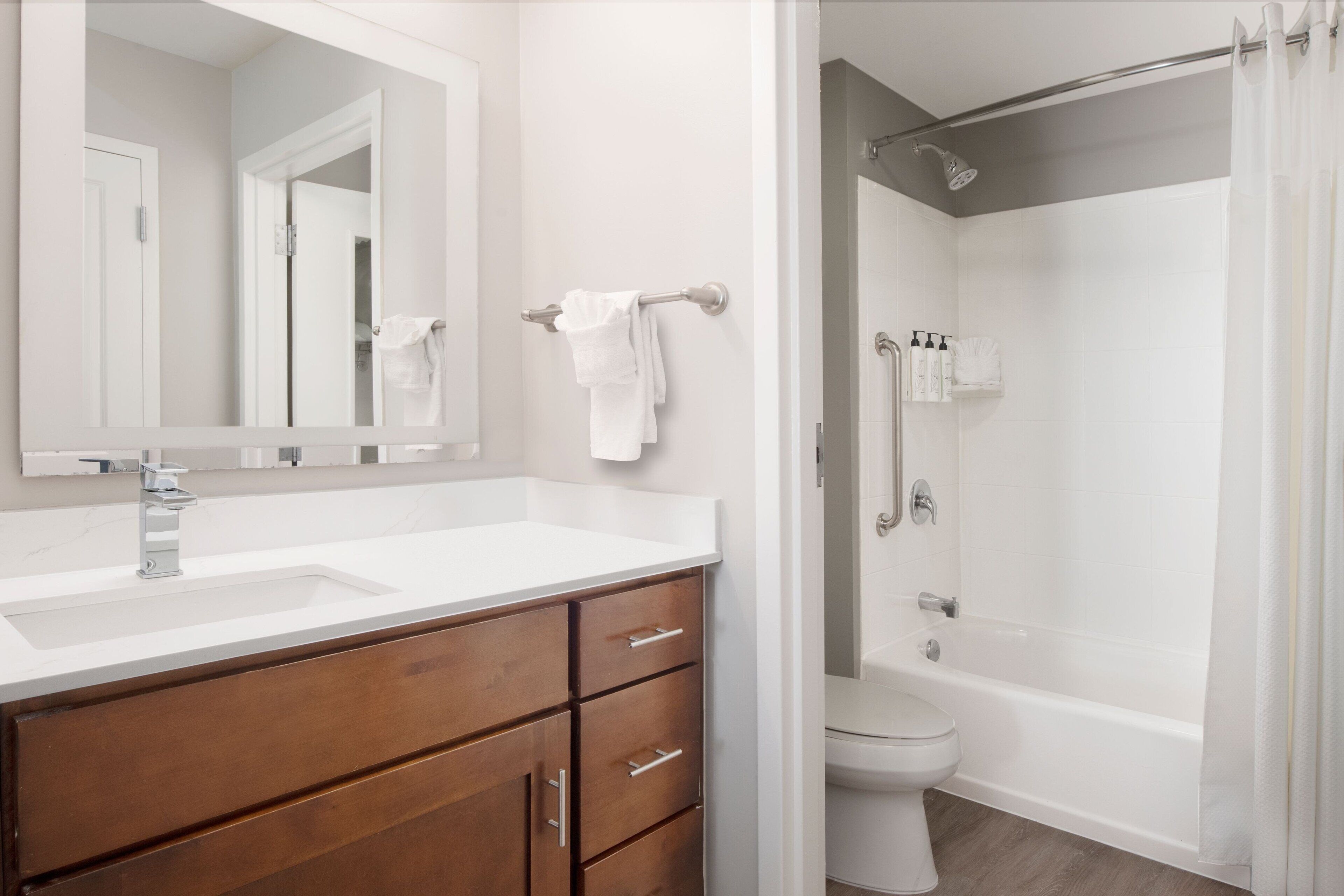 A bathroom with a white sink, wooden vanity, a large mirror, a toilet, and a shower area.