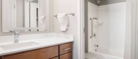 A bathroom with a white sink, wooden vanity, a large mirror, a toilet, and a shower area.