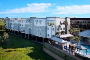 A multi-story hotel with a pool area, surrounded by greenery and palm trees. - TownePlace Suites by Marriott Galveston Island (Galveston)