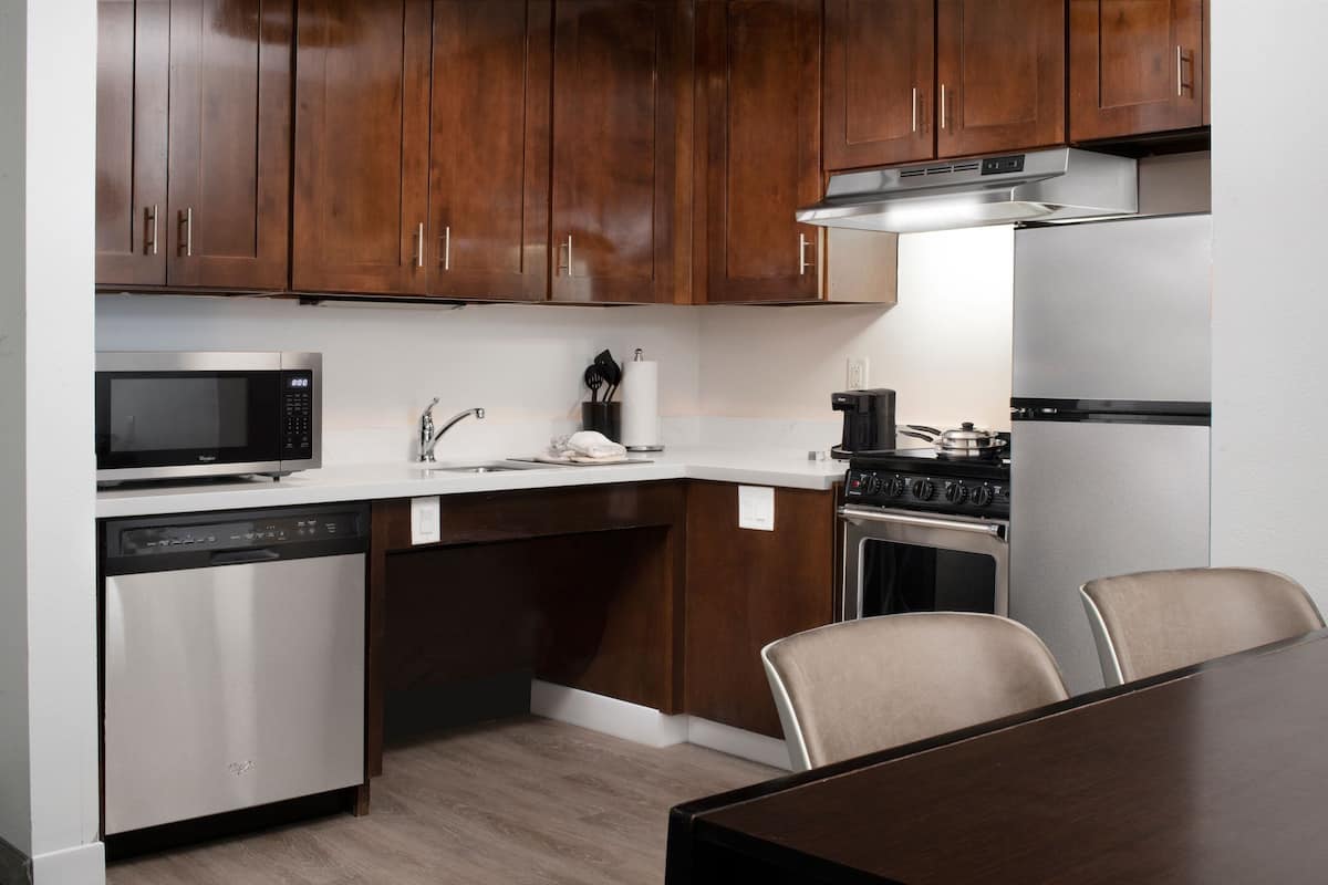 A modern kitchen with wooden cabinets, stainless steel appliances, and a dining area with a table and chairs.