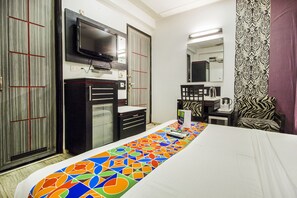 Ein Hotelzimmer mit Bett, Wandfernseher, Schreibtisch mit Stuhl und einem gemusterten Vorhang.