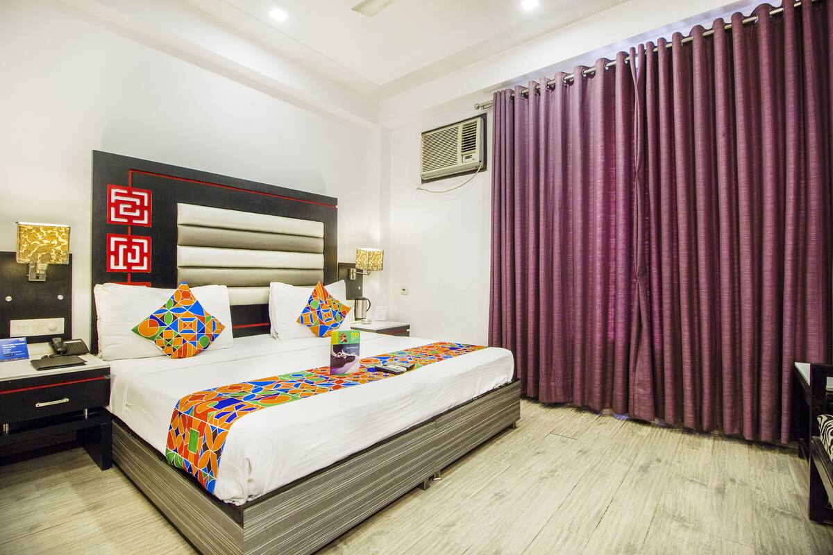 A hotel room with a large bed, a nightstand, a desk, and a window with purple curtains.