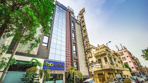 Un edificio de varios pisos con fachada de vidrio moderna, un cartel con el nombre 'Fabi Hotels', y un edificio tradicional con un cartel que dice 'Hotel'.