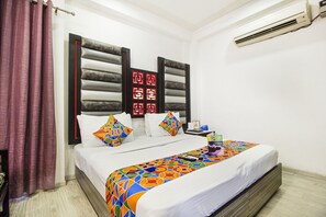 Ein Hotelzimmer mit Bett, Nachttisch, Lampe und einem Fenster mit Vorhängen.