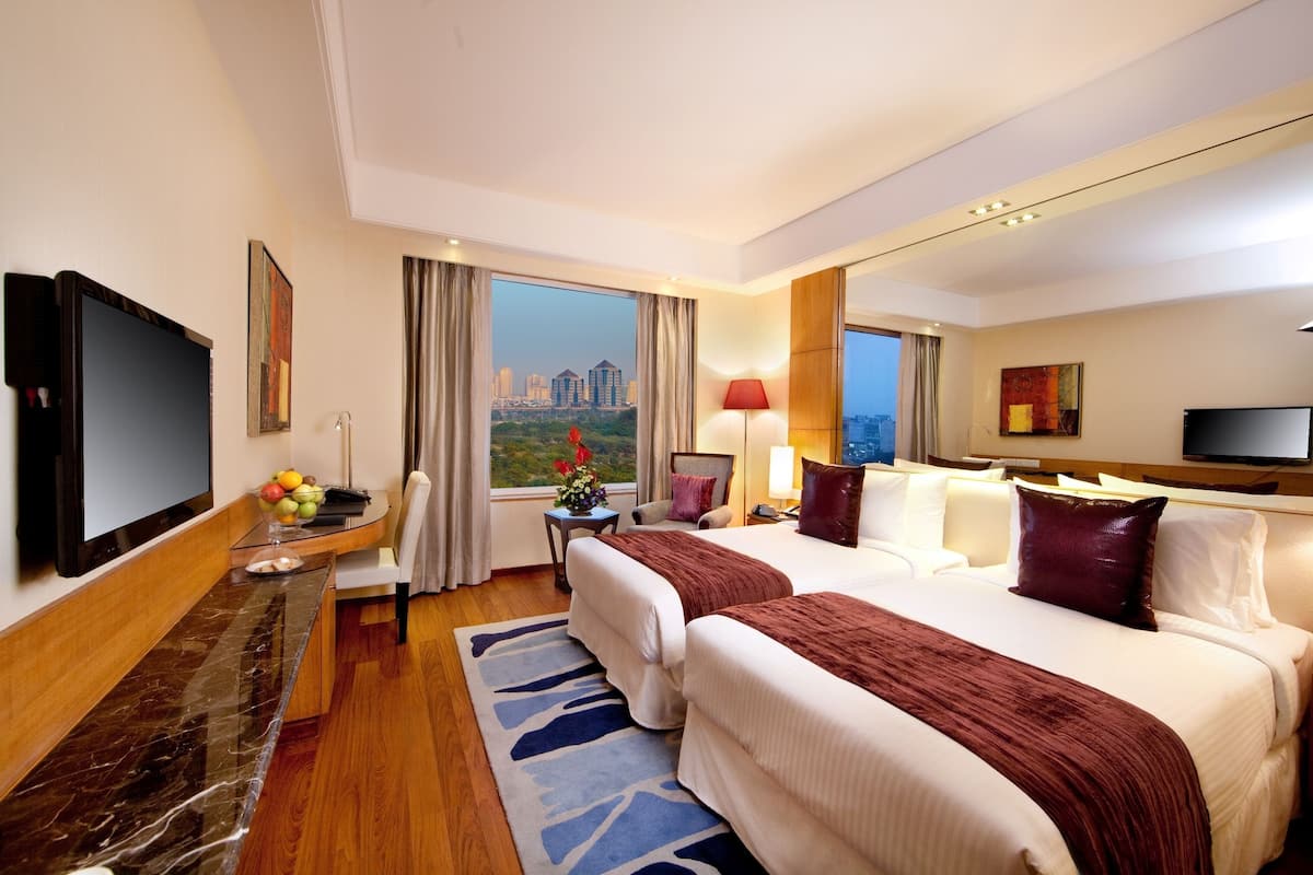 A hotel room with a large bed, a desk with a flat-screen TV, a city view, and a modern design.