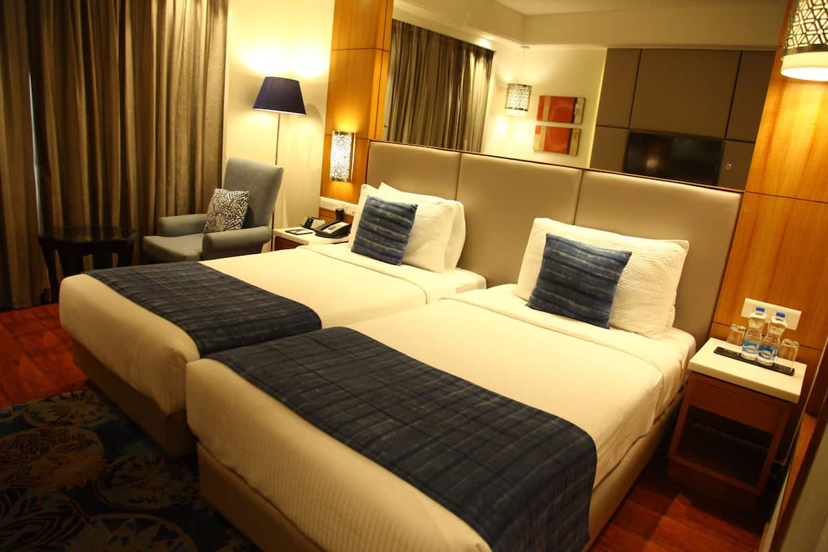 A hotel room with two beds, a chair, a nightstand, and a TV.