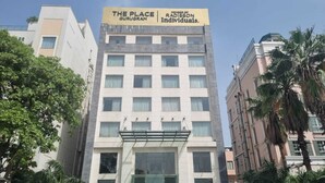 Ein mehrstöckiges Hotel namens "The Place Gurugram" mit moderner Fassade, großen Fenstern und einem Flachdach.