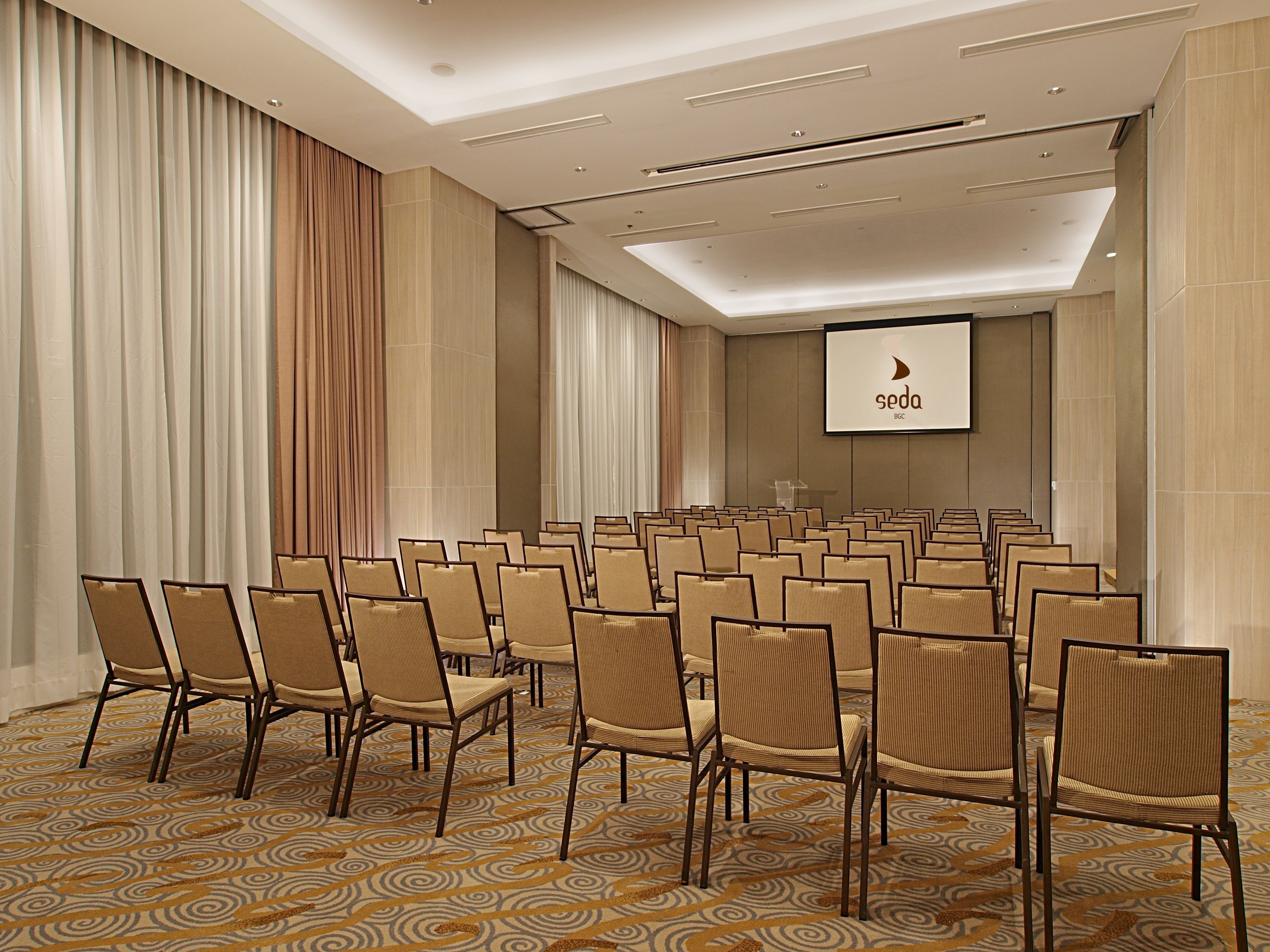 A conference room with rows of chairs, a large screen, and a patterned carpet.