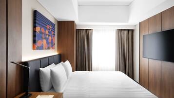 A modern hotel room with a large bed, a flat-screen TV, a desk with a lamp, and a painting on the wall.