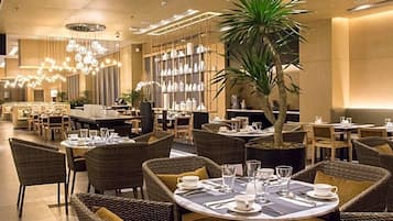 A restaurant with wicker furniture, tables set with white plates, glasses, and cutlery.