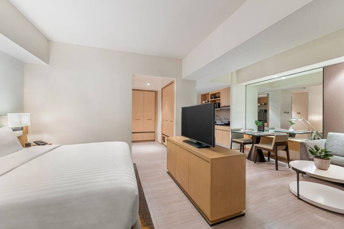 Ein modernes Hotelzimmer mit einem Bett, einem Fernseher auf einer Holzkommode, einem Schreibtisch mit Stuhl und einem Essbereich mit Tisch und Stühlen.