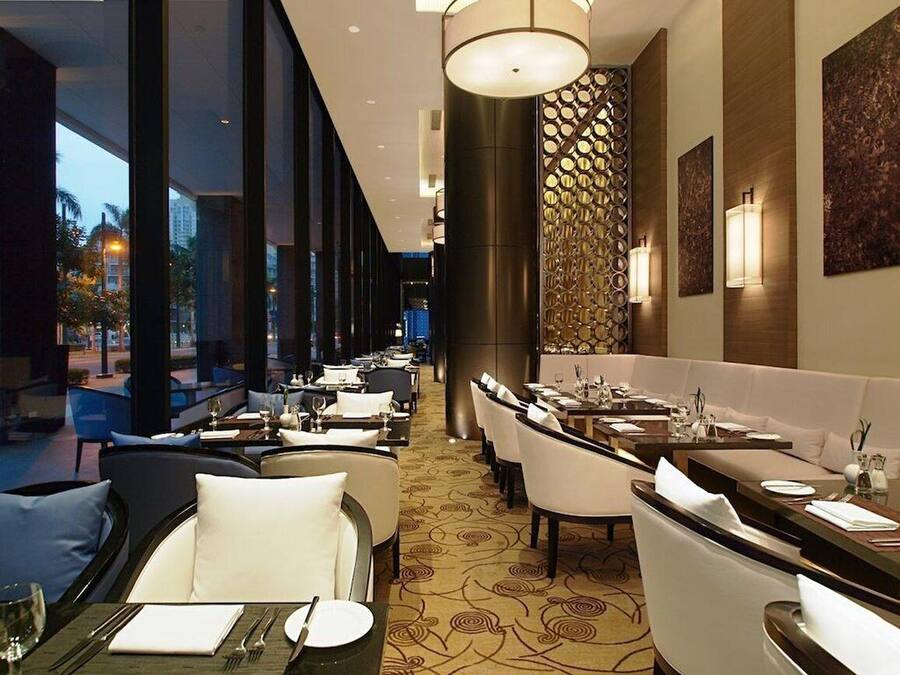 Un restaurante moderno con una barra larga, sillas blancas tapizadas y una alfombra estampada.