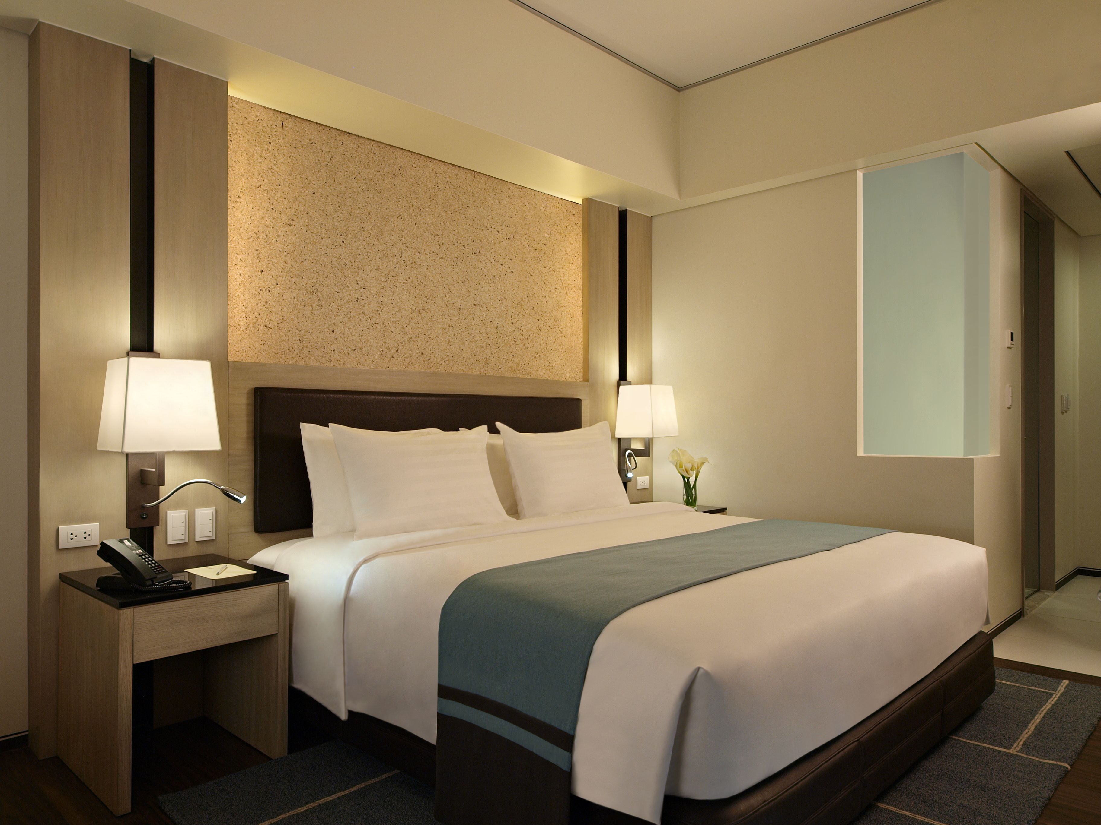 A hotel room with a bed, bedside lamps, a desk with a telephone, and a nightstand.