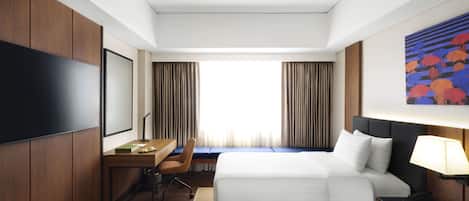 Habitación de hotel con dos camas, un escritorio, una silla, un televisor y un cuadro en la pared.