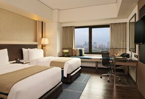 Habitación de hotel con dos camas, un escritorio, una silla, un televisor y vistas a la ciudad.