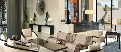 A modern lobby with a reception desk, seating area, and large windows offering city views.