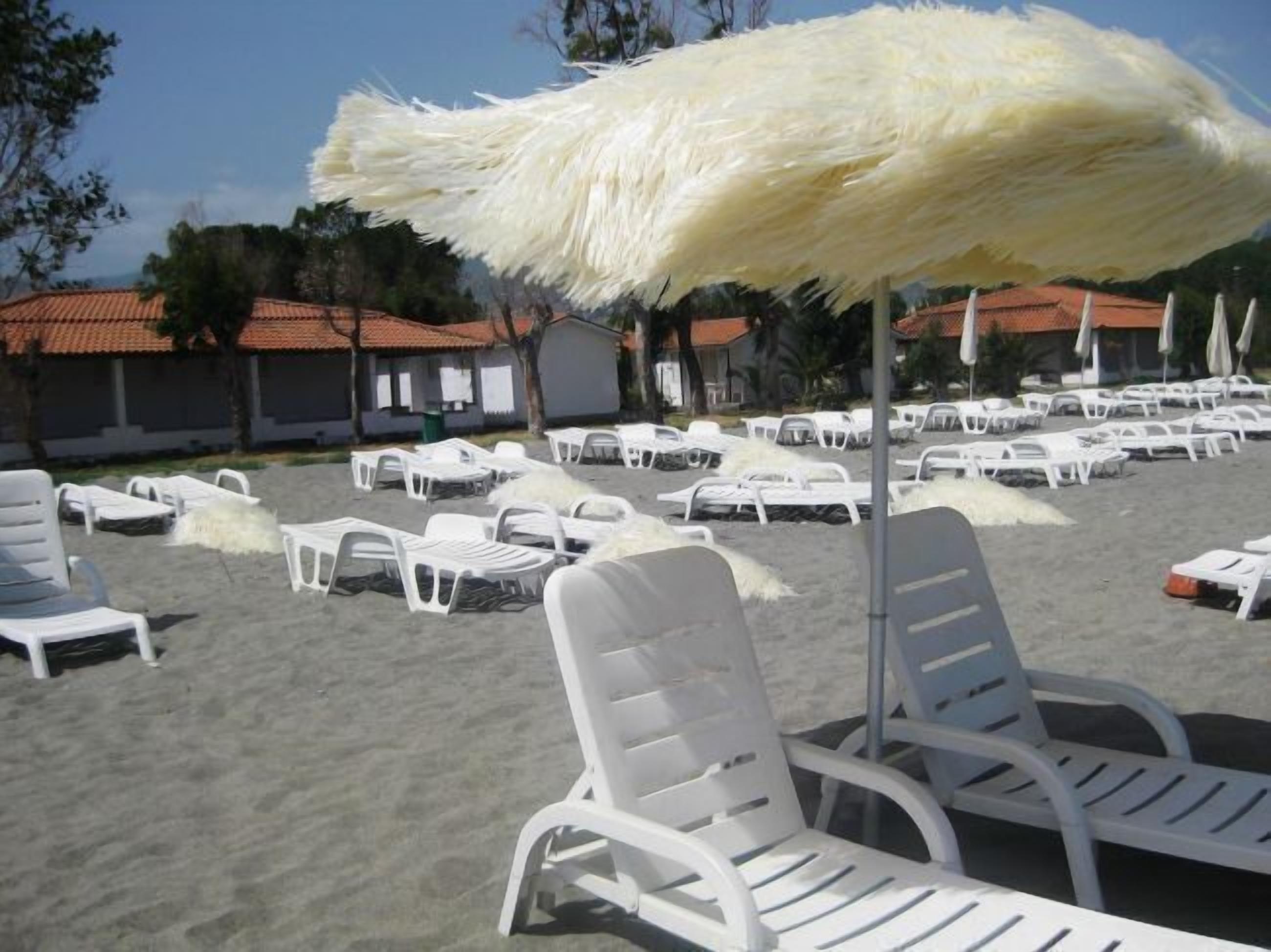 A beach area with white lounge chairs and a large white umbrella.