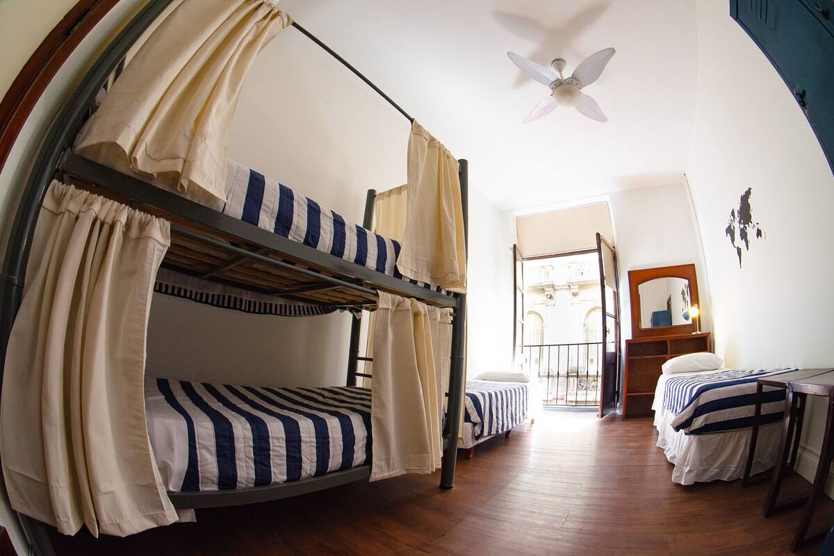 A bunk bed room with a ceiling fan, wooden flooring, and a small table.