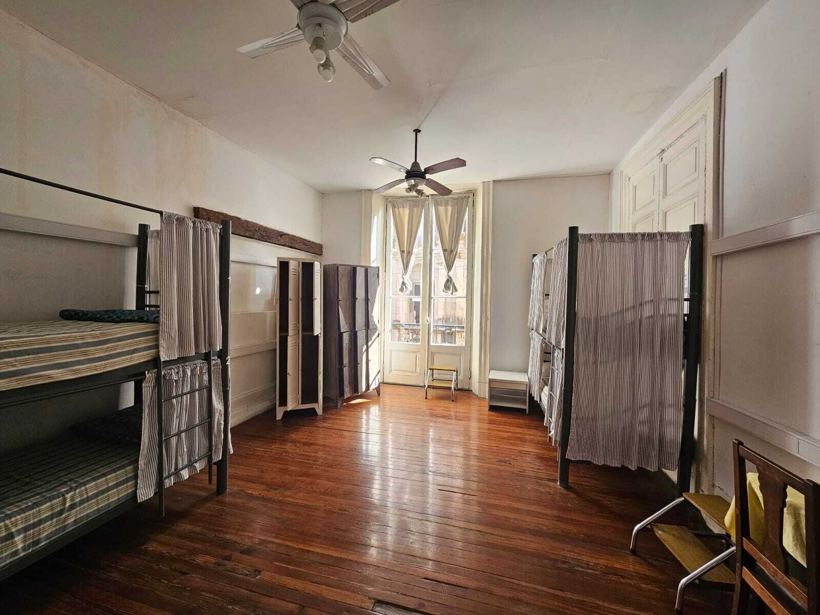 Un dormitorio con literas, un ventilador de techo y vistas a través de una ventana con cortinas.