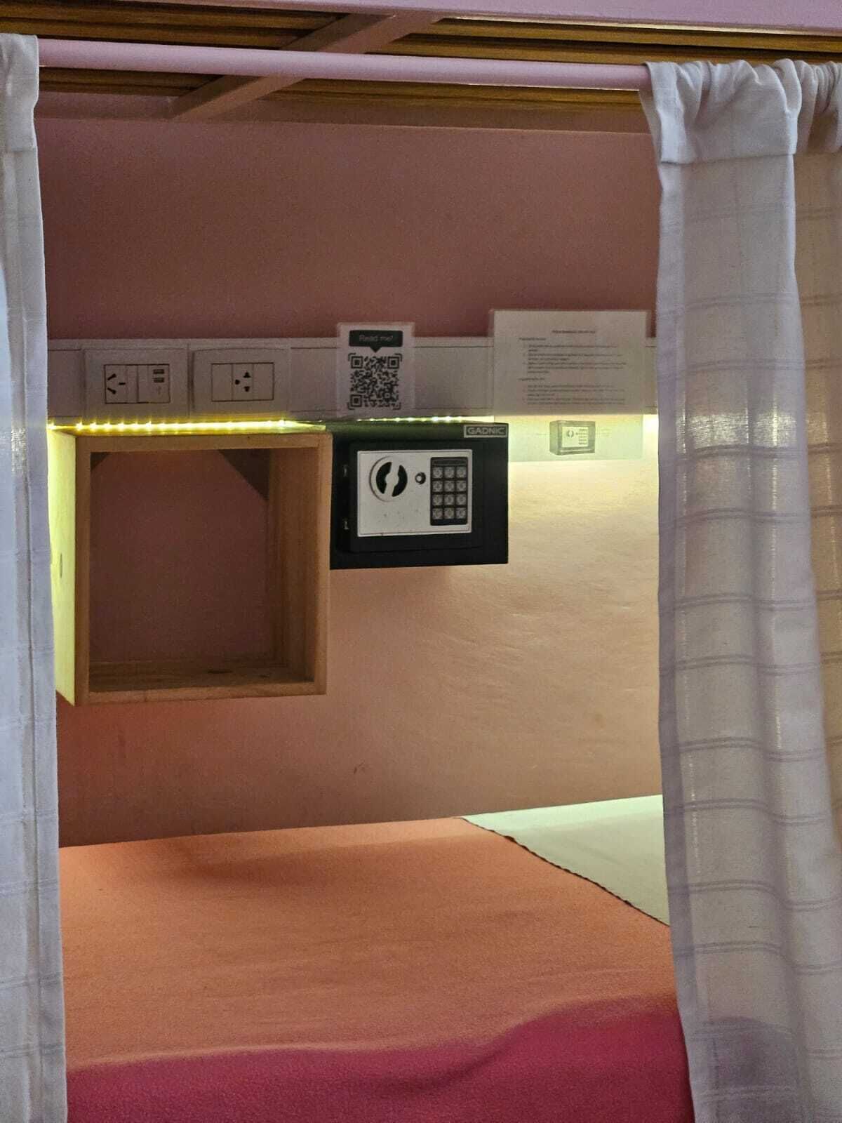Una habitación con cama, mesita de noche, panel de control en la pared y un código QR.