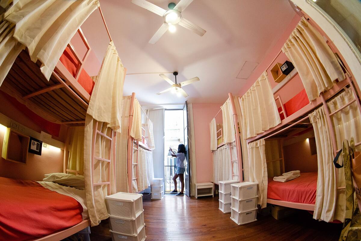 A dormitory room with bunk beds, a ceiling fan, and a window.