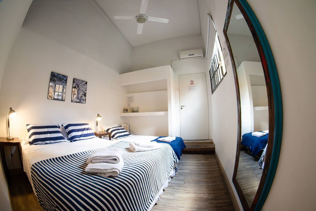 A hotel room with a large bed, two smaller beds, a ceiling fan, and a mirror.