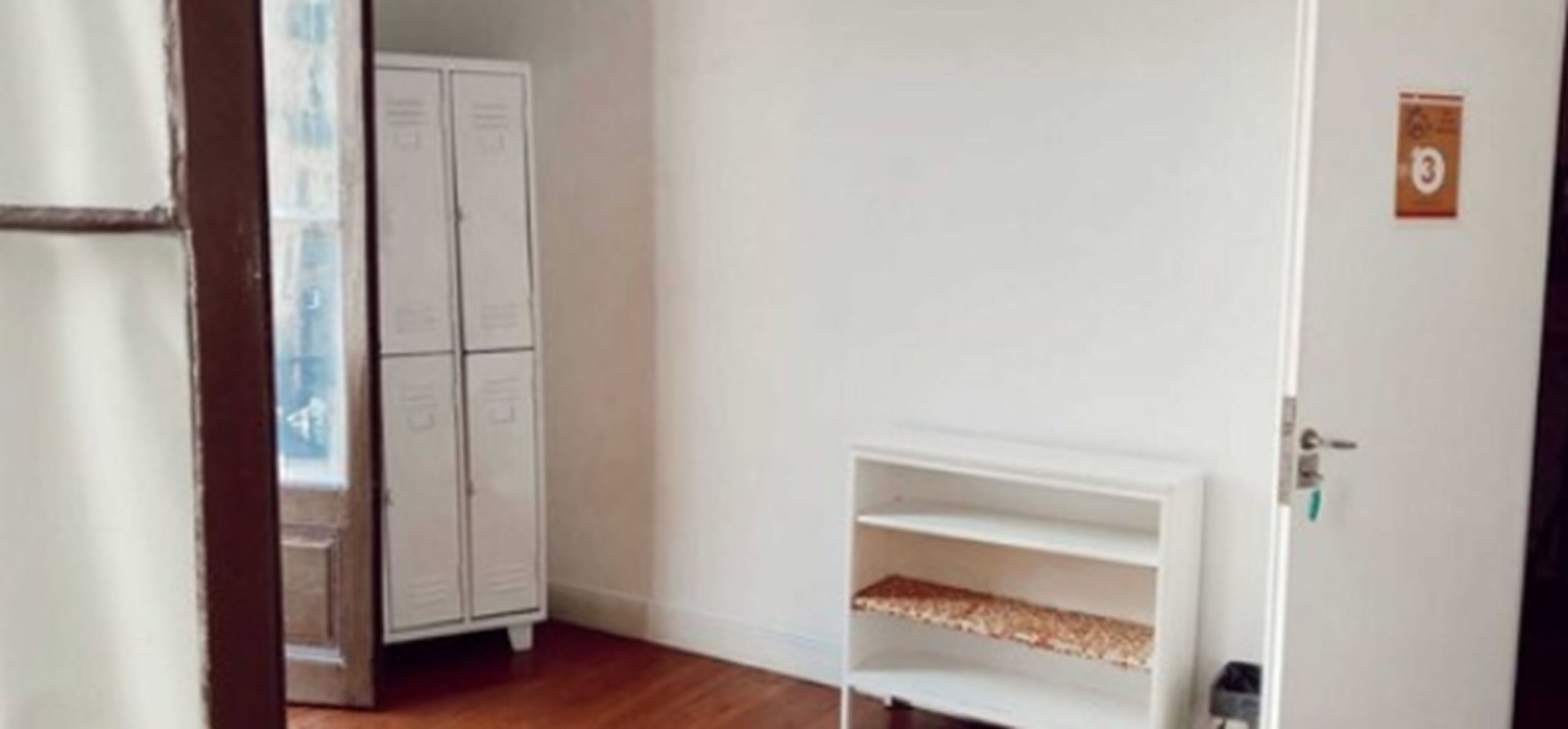 A room with a wooden floor, a white wardrobe, and a white shelf unit.