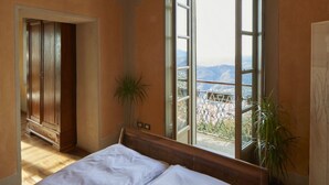 A bedroom with a large bed, a view of the mountains through a large window, and a potted plant. - Bellavista Boutique Hotel (Brunate)
