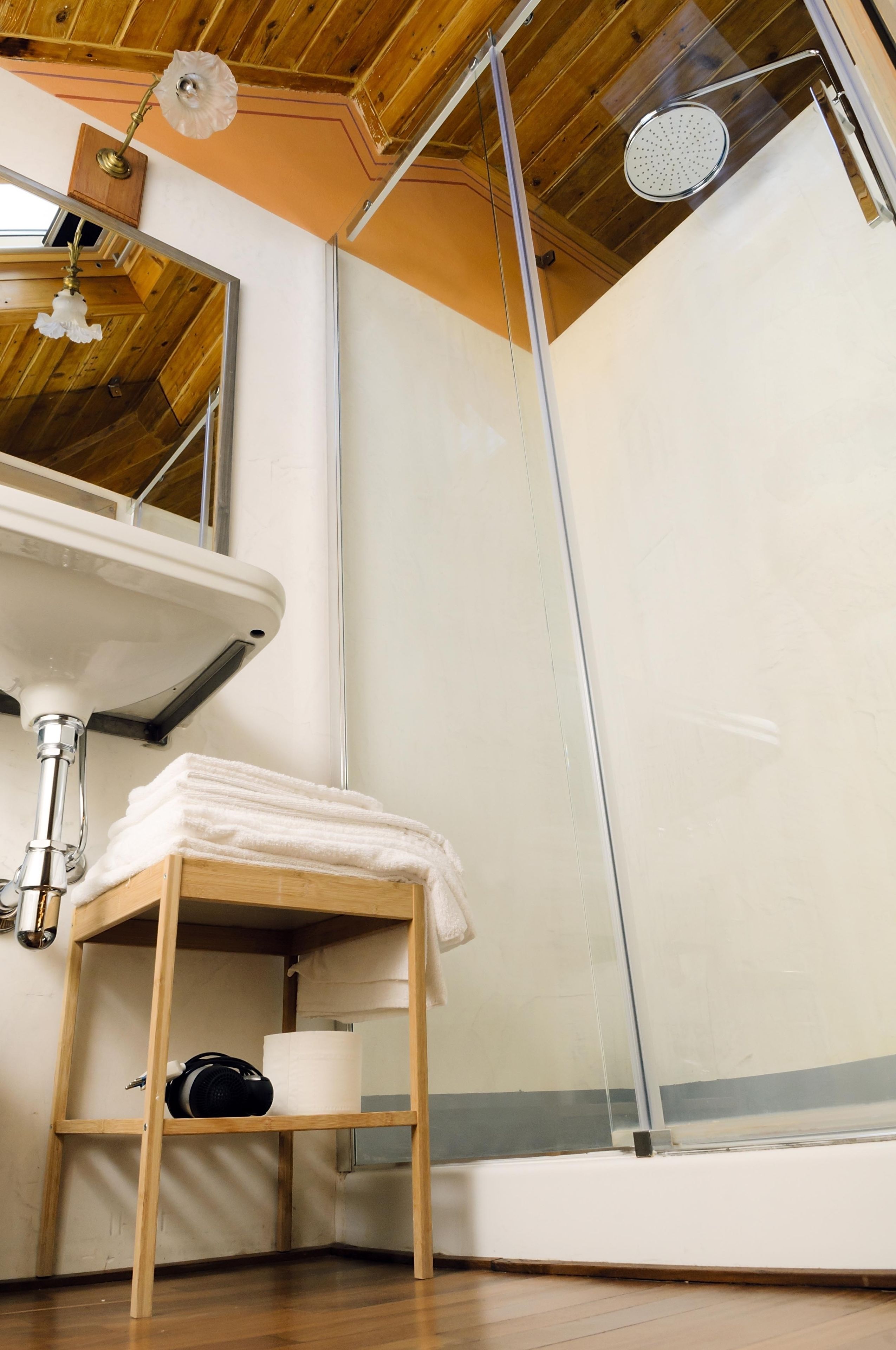 A bathroom with a wooden ceiling, a sink, a towel rack, and a shower enclosure.