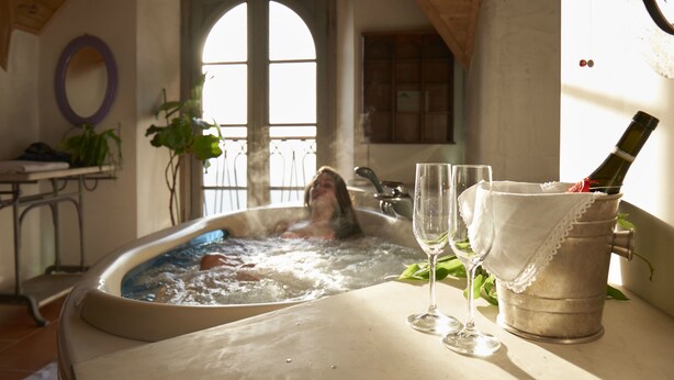 A hot tub with a person in it, two glasses, and a bottle of champagne on a table. - Bellavista Boutique Hotel (Brunate)