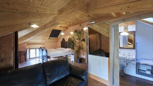 A cozy attic bedroom with a wooden ceiling, a black leather sofa, a bed, and a bathroom with a sink and mirror. - Bellavista Boutique Hotel (Brunate)