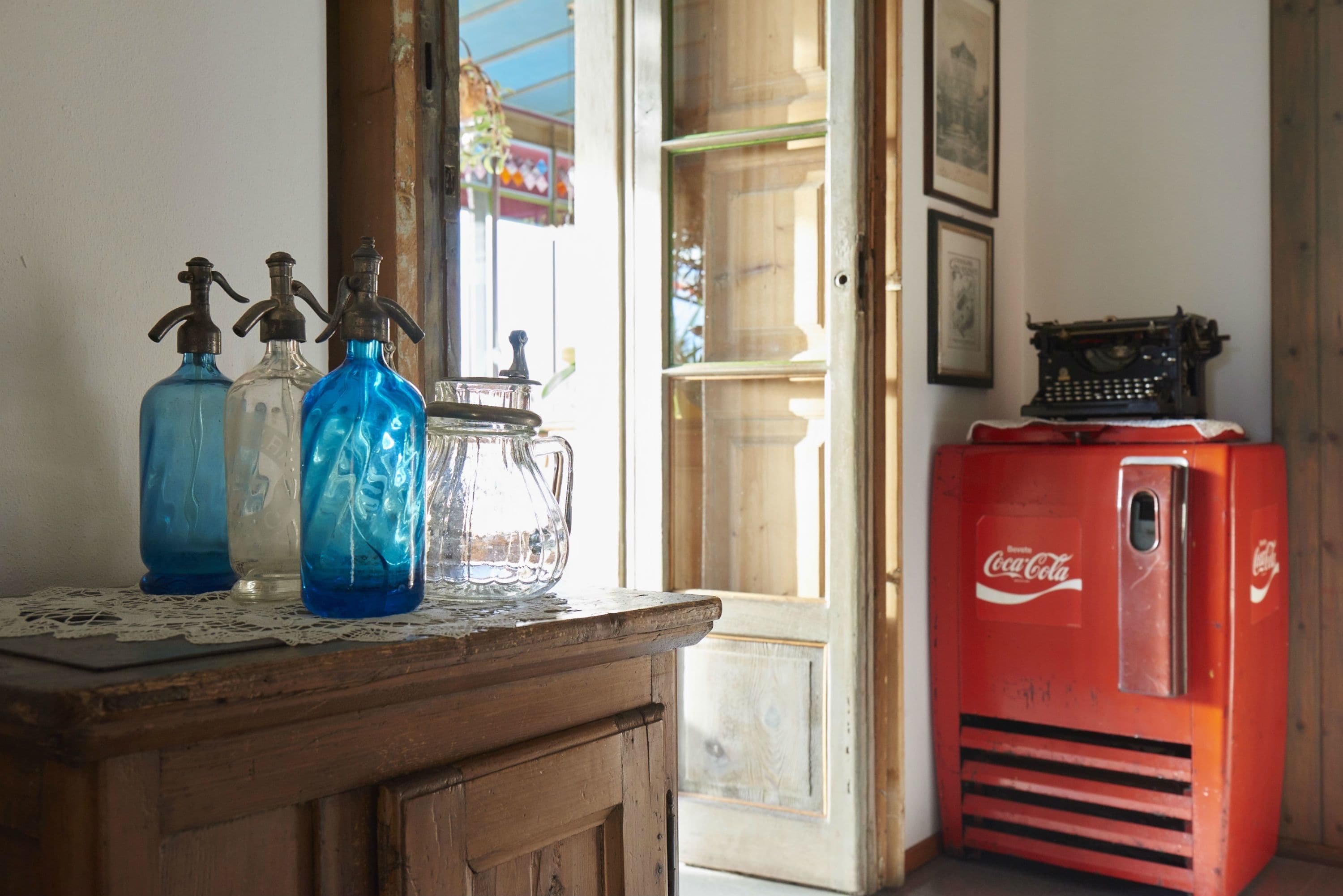 Ein Holzkabinett mit einem alten Coca-Cola-Kühlschrank, klaren Glasflaschen und einem Metallkrug.