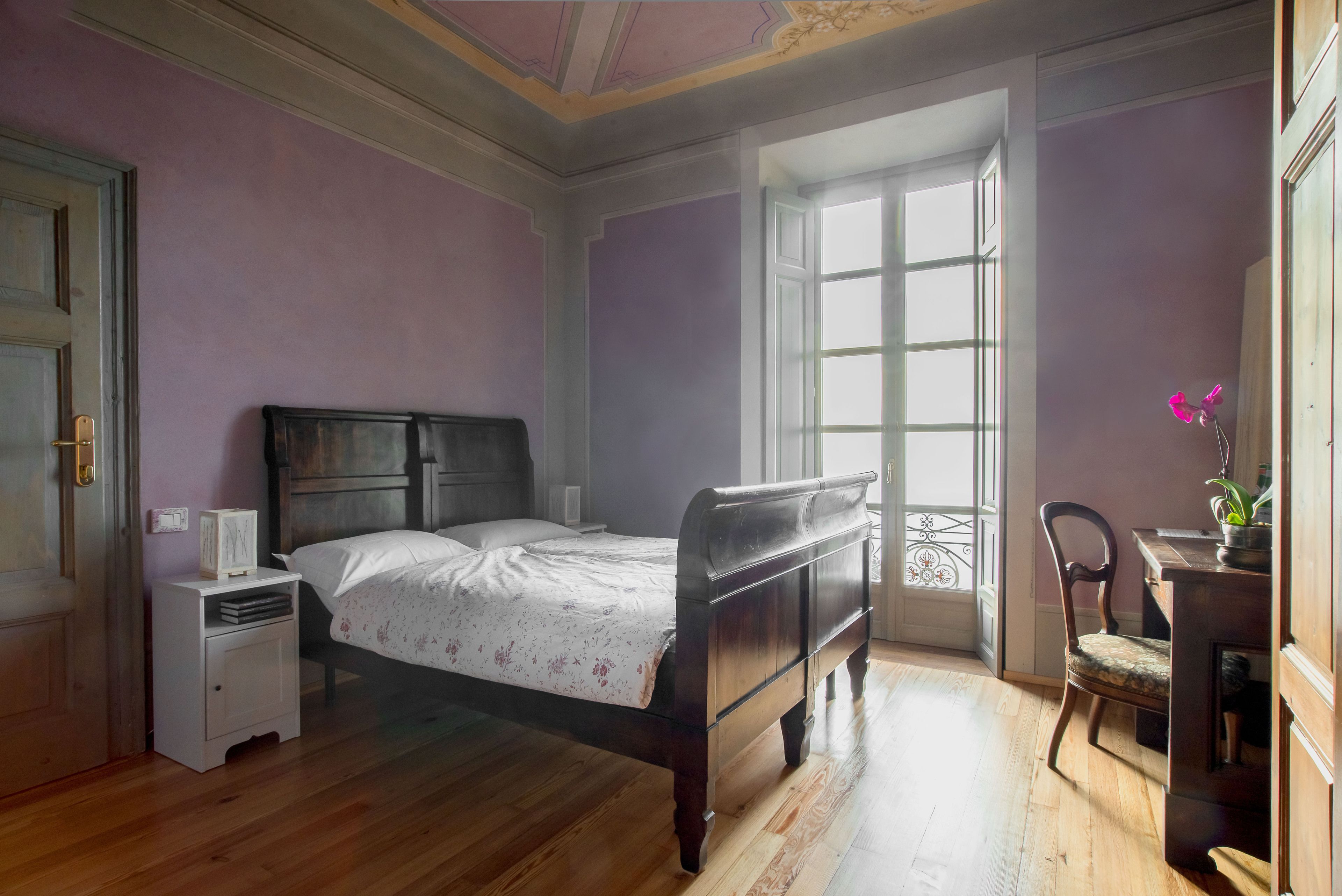 Ein Schlafzimmer mit einem Holzbett, einem Nachttisch, einem Sessel und einem Fenster mit Blick.