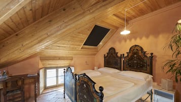 Une chambre avec un plafond en pente, un cadre de lit en bois, une table de chevet et une commode, ainsi qu’une fenêtre.