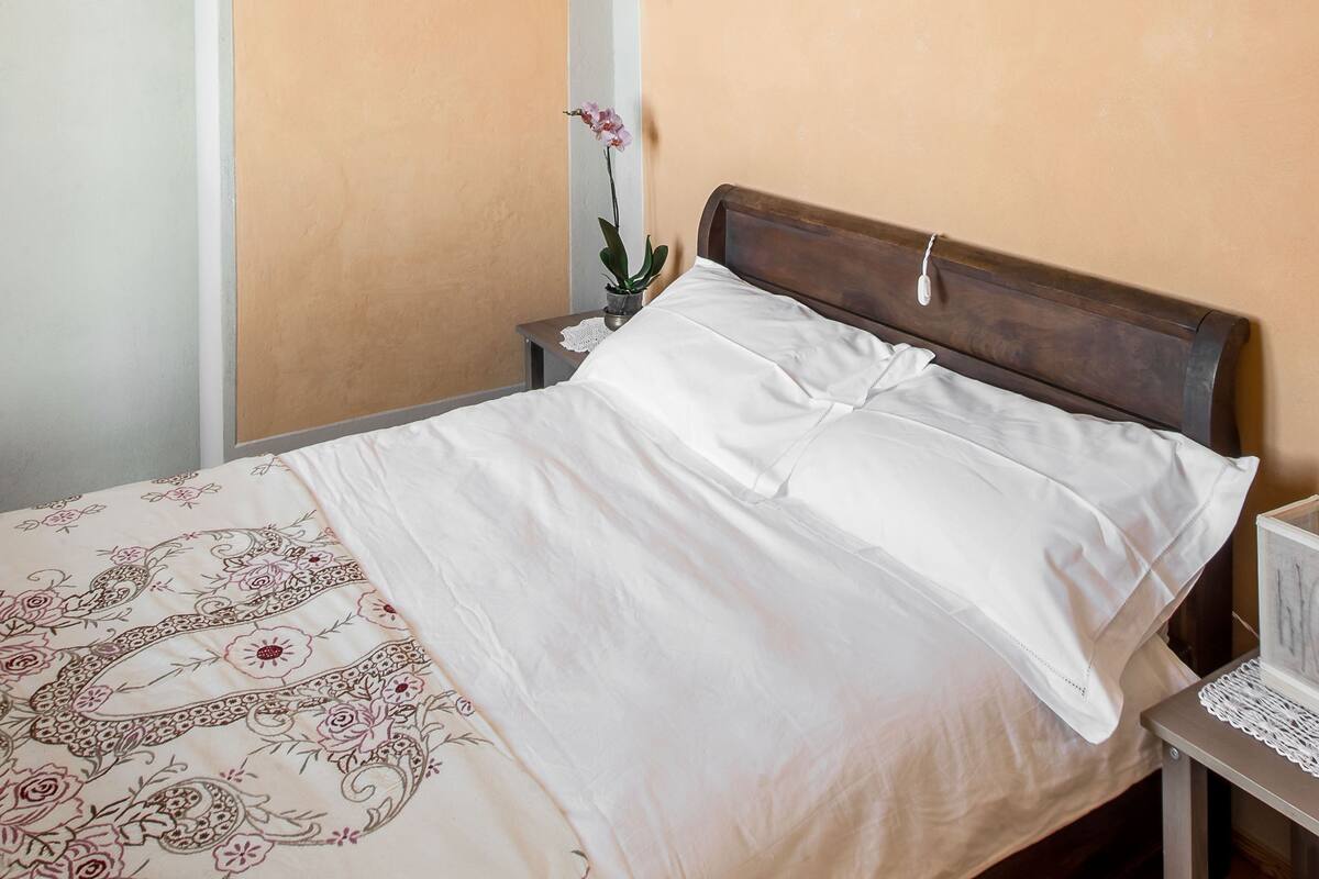 Une chambre à coucher avec un lit, une table de chevet, un vase avec une fleur et un plafond orné d’un motif géométrique.