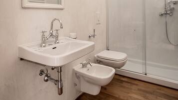 A modern bathroom with a white sink, bidet, and glass-enclosed shower.