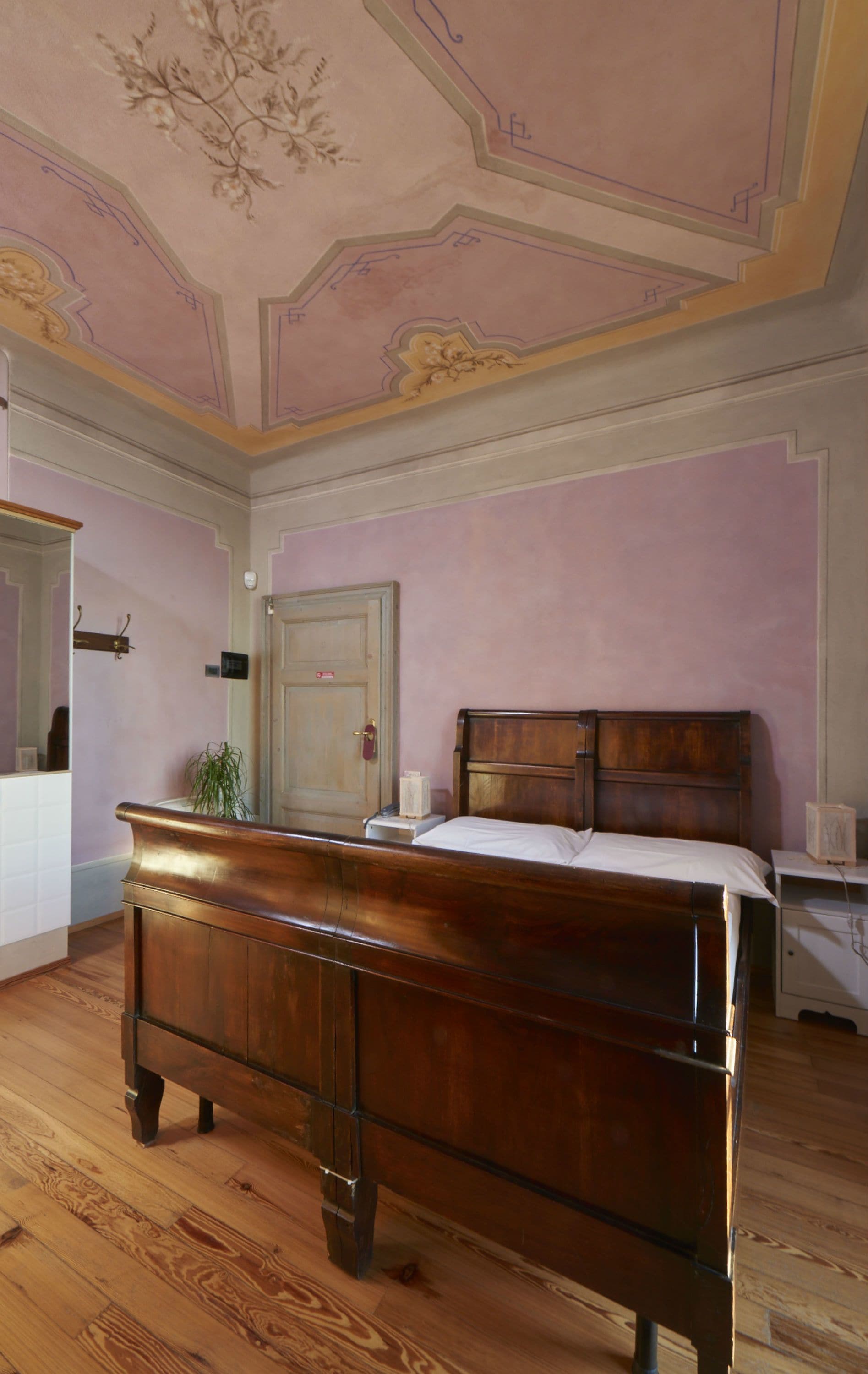 Un dormitorio con una cama de madera, una mesita de noche, un aparador, un espejo y una puerta.