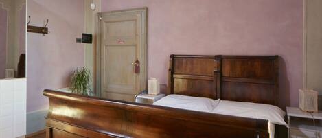 Un dormitorio con una cama de madera, una mesita de noche, un aparador, un espejo y una puerta.