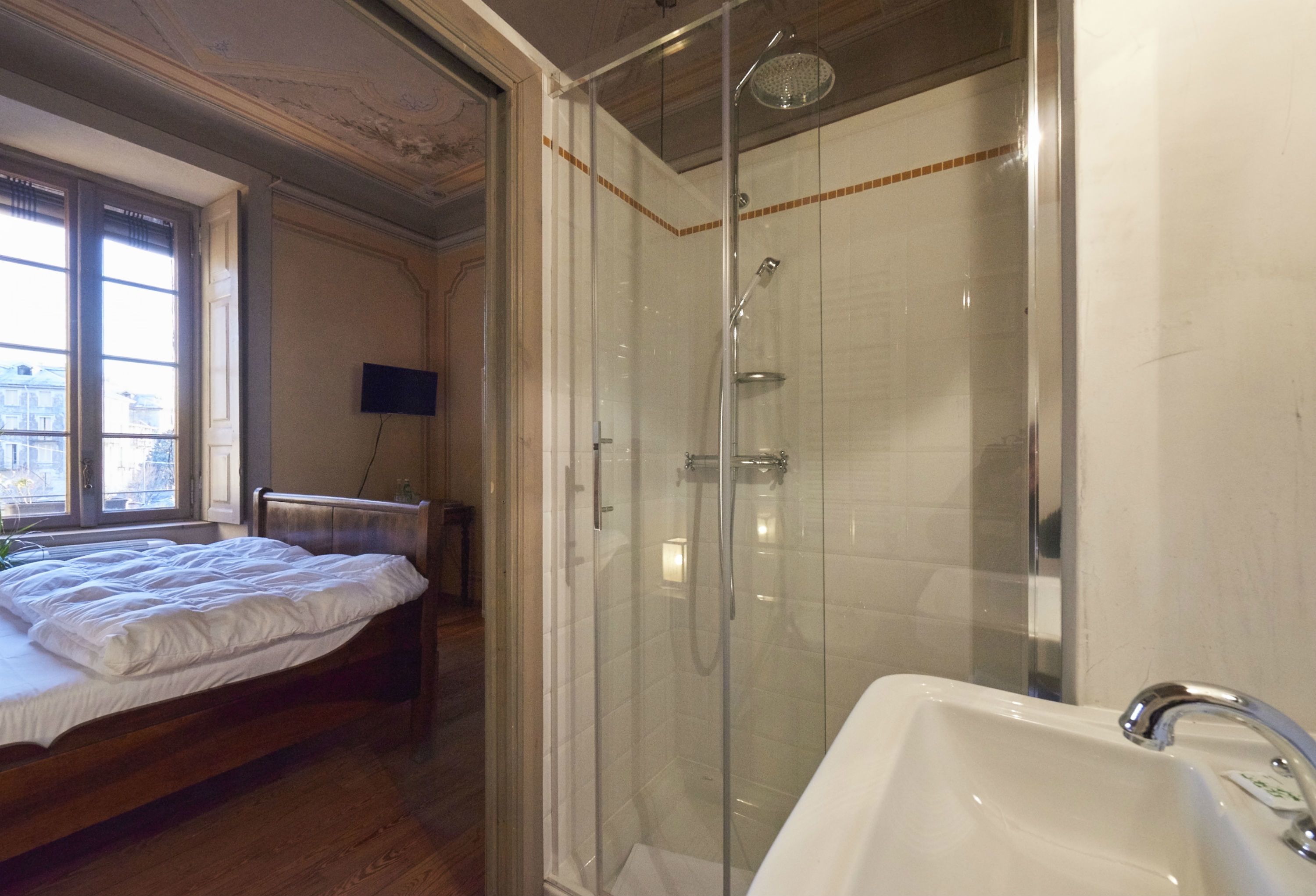 Un dormitorio con cama, ducha con puerta de cristal y baño con lavamanos.