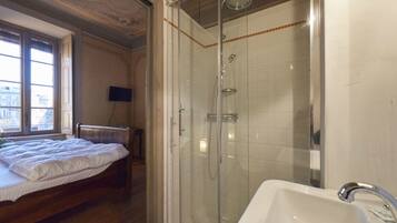 Un dormitorio con cama, ducha con puerta de cristal y baño con lavamanos.