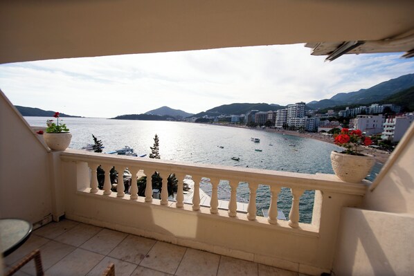 A balcony with a view of a calm sea, boats, and buildings in the background. - New Hotel Kuc By Marvel (Becici)