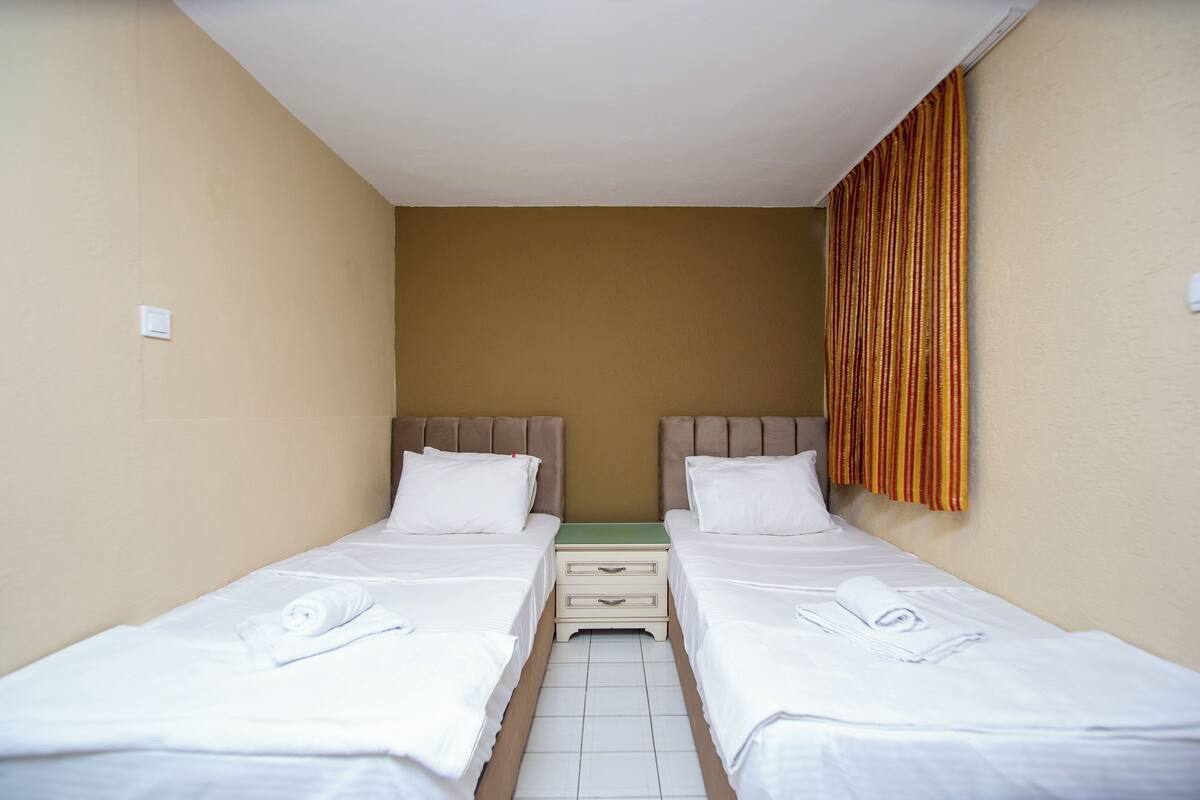 A twin room with two beds, a small bedside table, and a curtain on one wall.